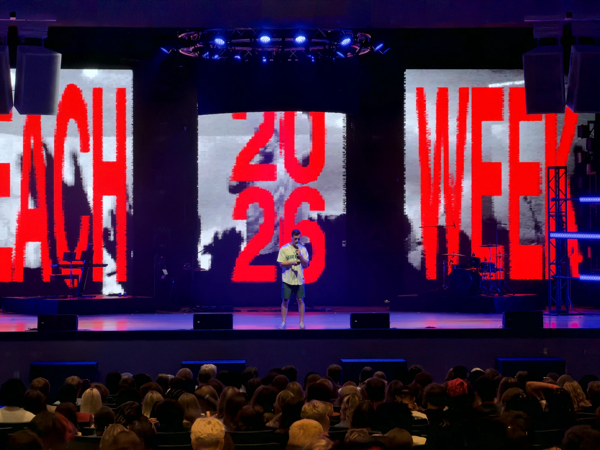 A single speaker at center stage under giant Beach Week typography, the crowd listening