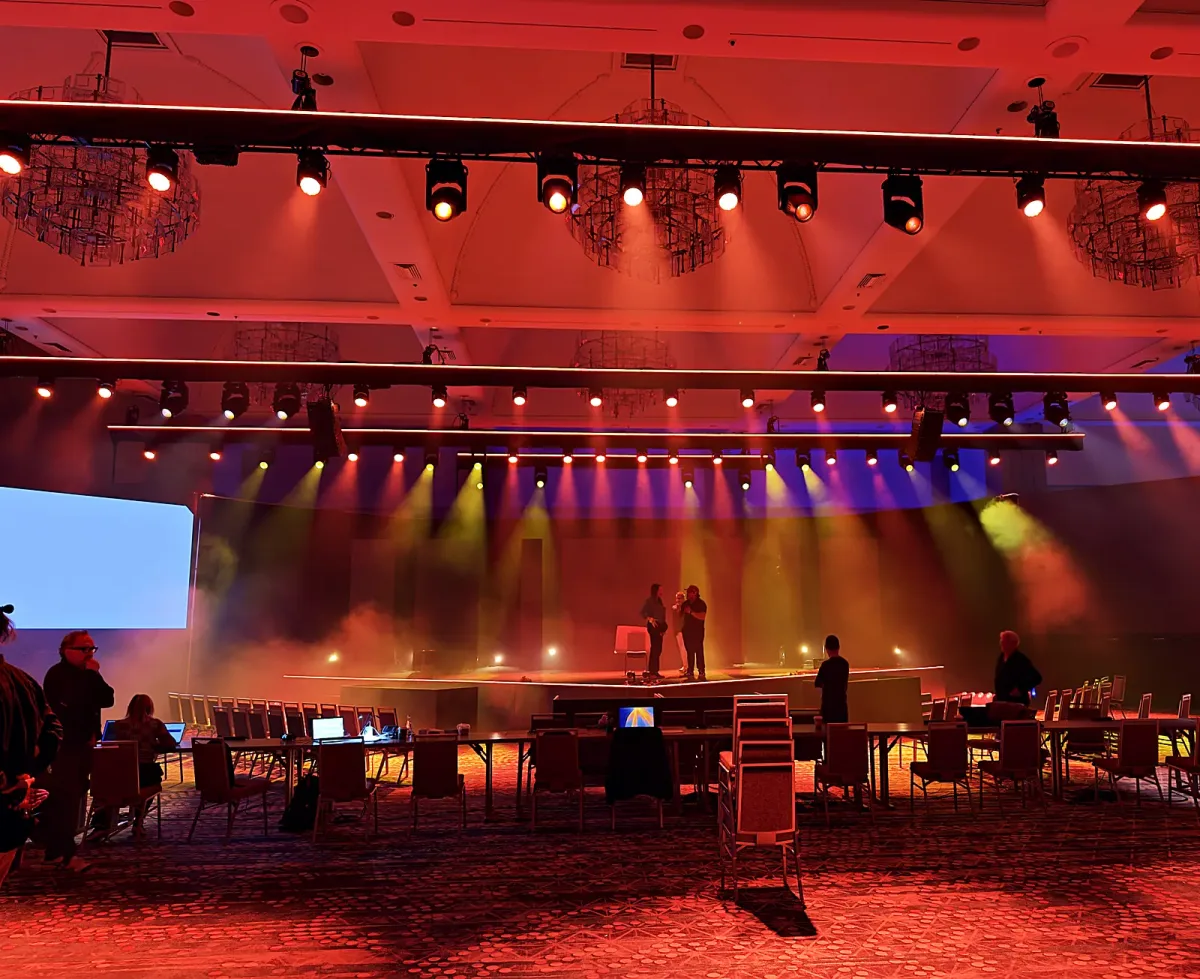 Amber rehearsal lighting over a general-session stage build in a hotel ballroom