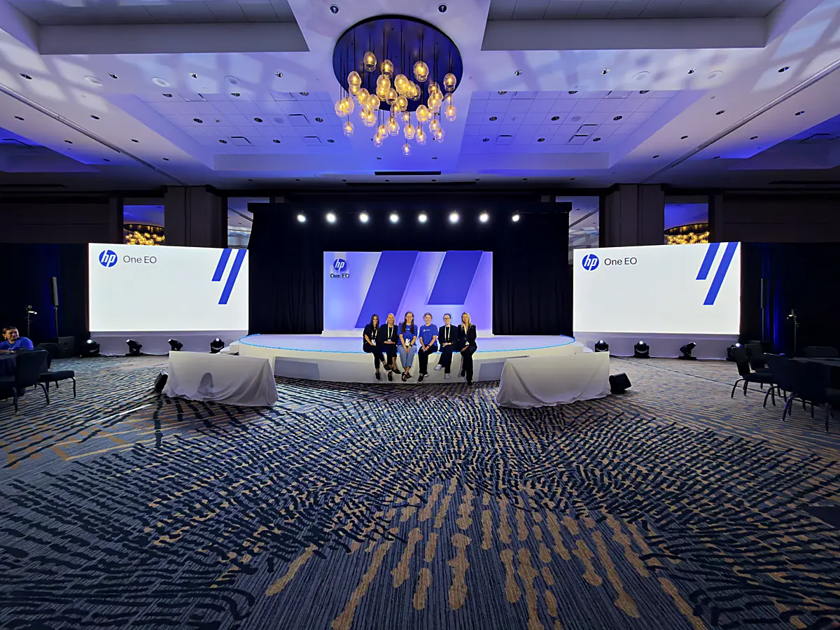 Custom half-circle stage and fabricated scenic wall carrying one event identity across stage and screens
