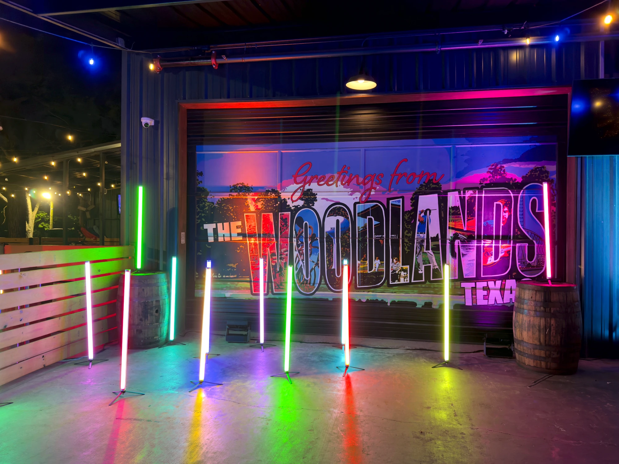 Neon Cowboy offsite: giant Greetings from The Woodlands Texas postcard backdrop with rainbow LED light tubes and whiskey barrels