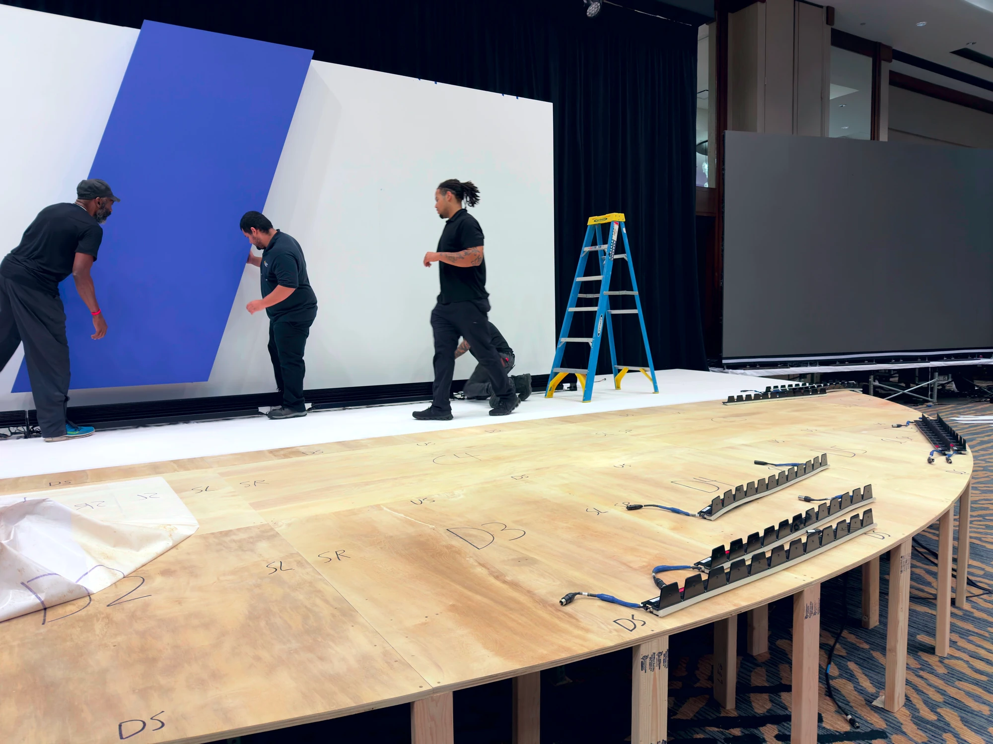 Crew installing the scenic wall behind the raw curved half-circle stage deck with position markers