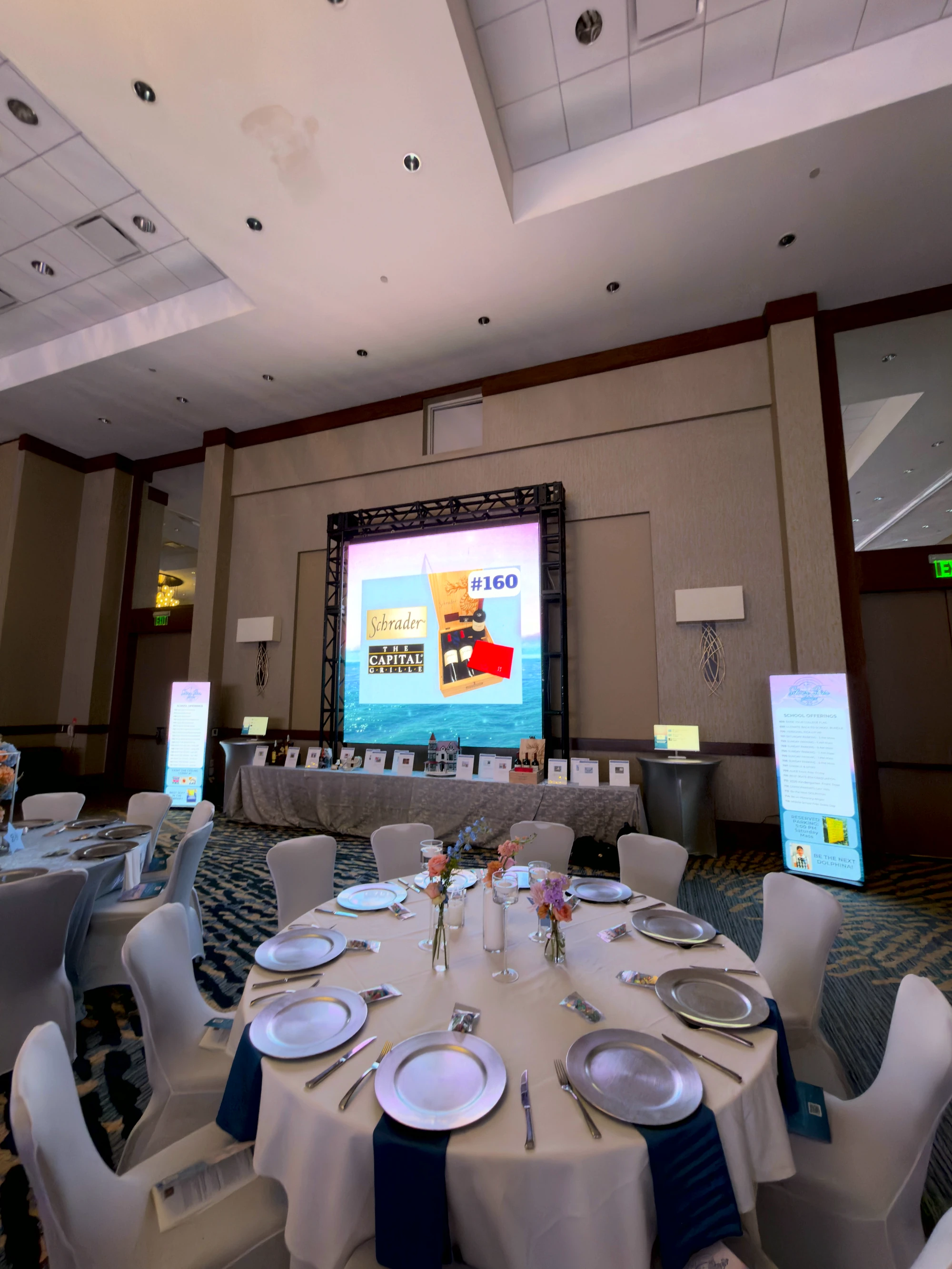 Auction lot on the big screen beside its staged display table and a set place setting