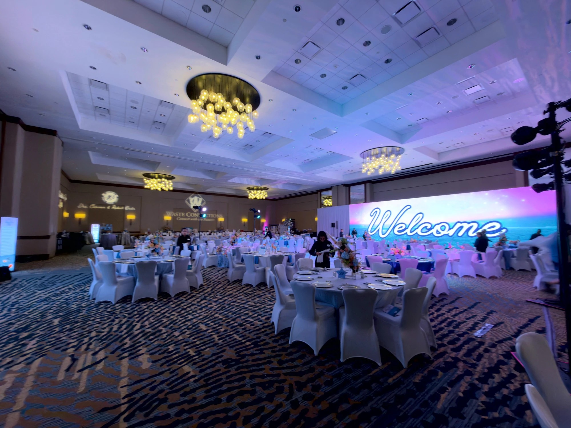Ocean-themed Welcome LED wall over round tables set in silver and blue